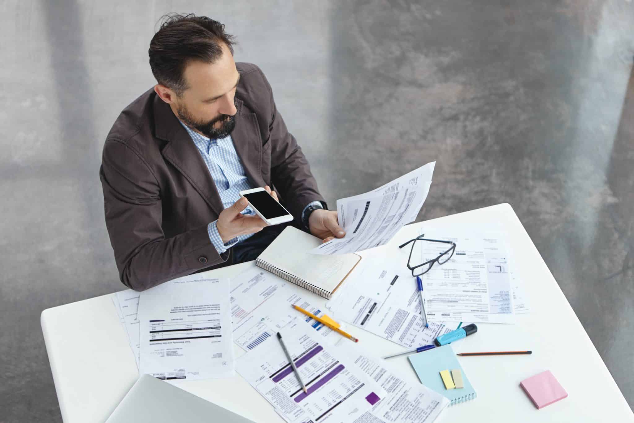 Male employee going over business reports and analysis. He is speaking on his phone at the same time